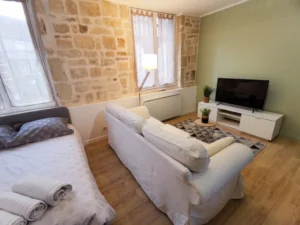 Vue plongeante sur l'agencement du séjour montrant le canapé confortable, la table basse filaire, le meuble TV blanc et la luminosité des fenêtres.